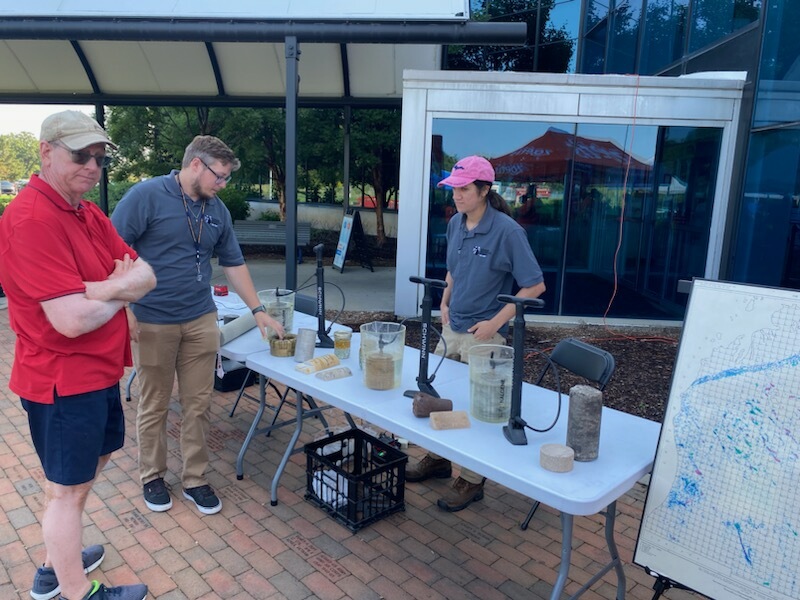 Photo of two staff members at educational booth, teaching about water well drilling using demonstration model