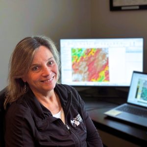 Linda Zabik sitting in front of a computer displaying Michigan topography.
