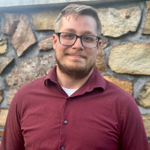 Matt Bell wearing a red shirt in front of a masonry rock wall.