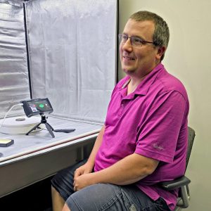 Rick Haagsma wearing a pink shirt sitting next to a 3D image booth.