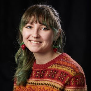Sam Zink wearing a multicolored sweater with a dark background.