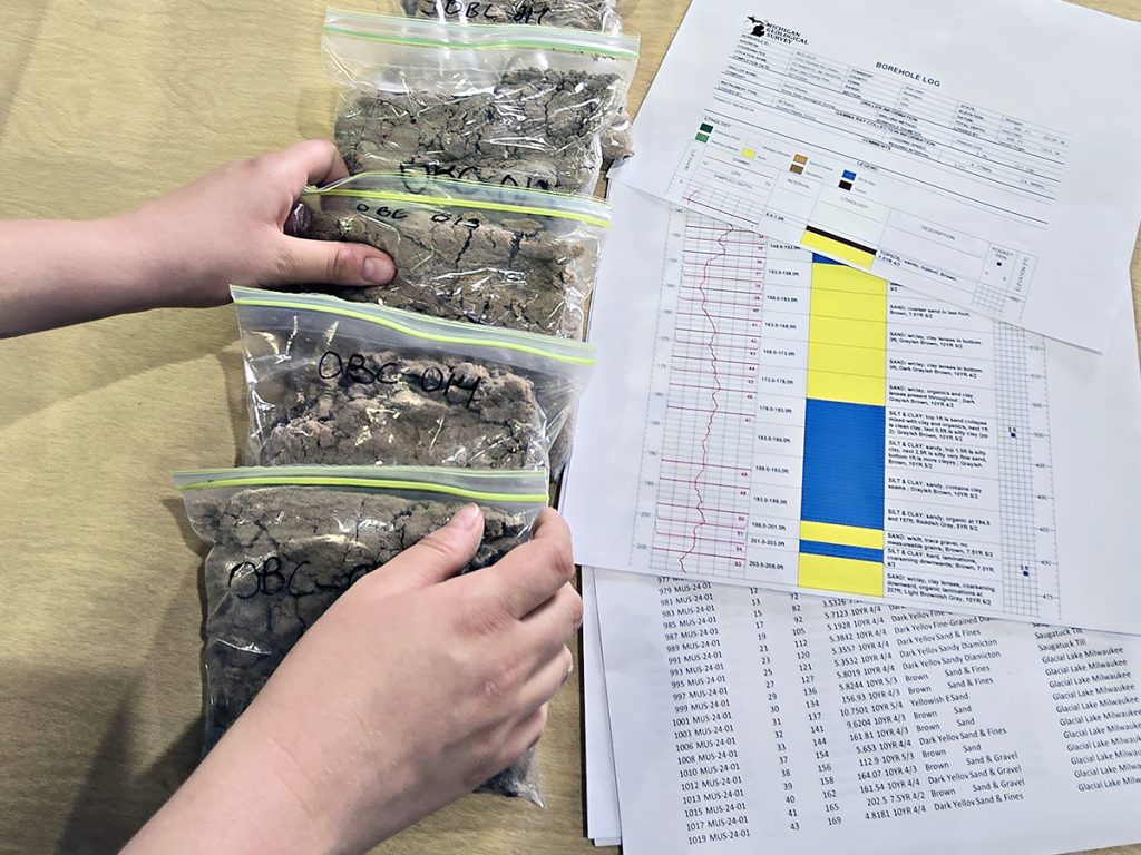 Sample bags of sediment set alongside borehole data logs.