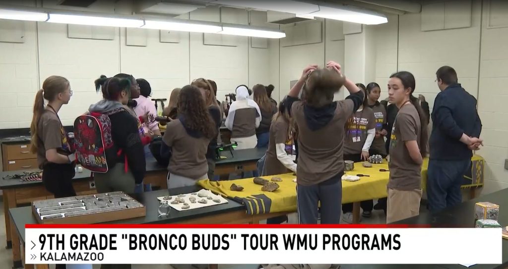 Group of 9th grade students examining rocks and fossils laid out on tables during WMU Bronco Buds tour.