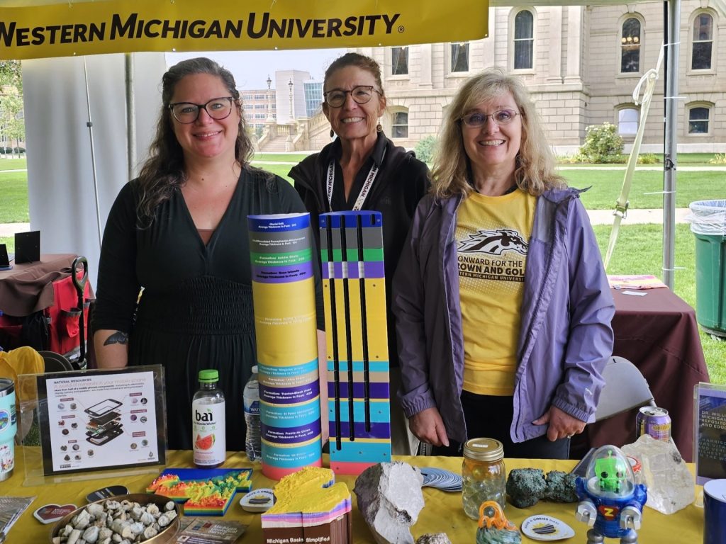 A group of women standing under a tent at a geology booth.