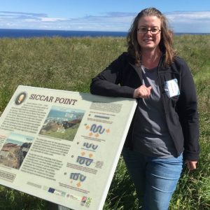 Amber Conner standing in a grassy area, leaning against a sign.