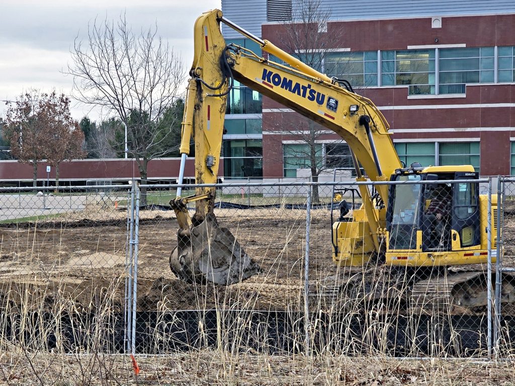 Yellow excavator behind a chain link fence on a construction site.