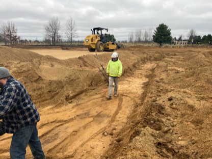 Construction photo of the new MGRRE site showing the subgrade with construction workers in the foreground and a heavy-duty roller in the background.