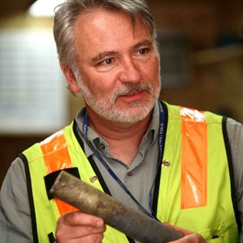 Bob Mahin wearing a yellow safety vest and holding an object while giving a presentation.