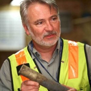 Bob Mahin wearing a yellow safety vest and holding an object while giving a presentation.