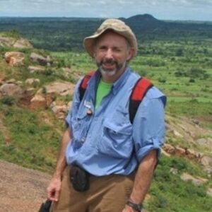 John Esch wearing a hat and blue shirt outdoors with a grassy plain in the background.