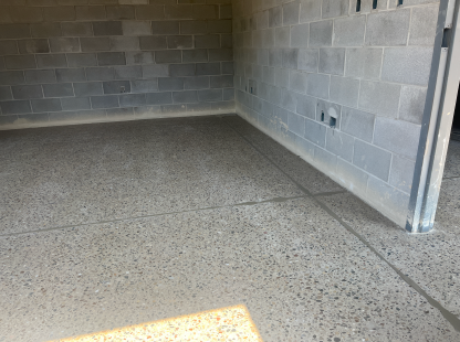 Finished polished concrete floor inside a concrete block building, with construction equipment, extension cords, and unfinished doorways leading to adjacent rooms under active interior construction.