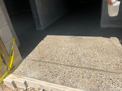 Polished concrete entry threshold leading into an unfinished concrete block building, with exposed aggregate flooring extending through interior doorways and caution tape marking ongoing construction work.